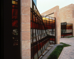 With its artfully orchestrated stripes, Claire Falkenstein’s stained glass windscreen creates a playful counterpoint to the solemn vertical rise of the adjacent buildings. The horizontal bands of sunset hues convey continuity, while the staggered vertical lines lend a jaunty spirit. Falkenstein is known for her massive glass and metal sculptures related to architecture.